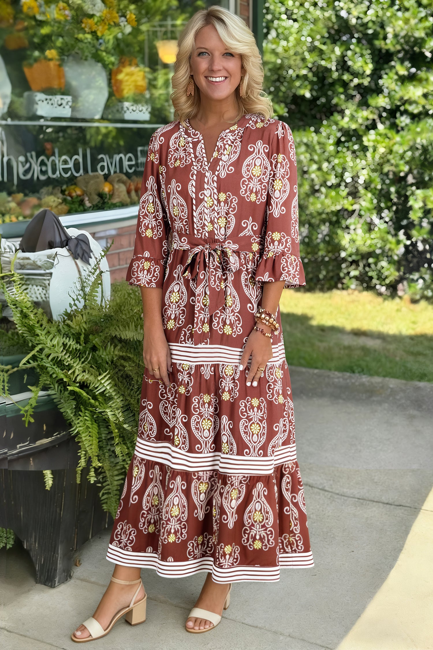 Woman wearing a red patterned dress standing outdoors with greenery in the background